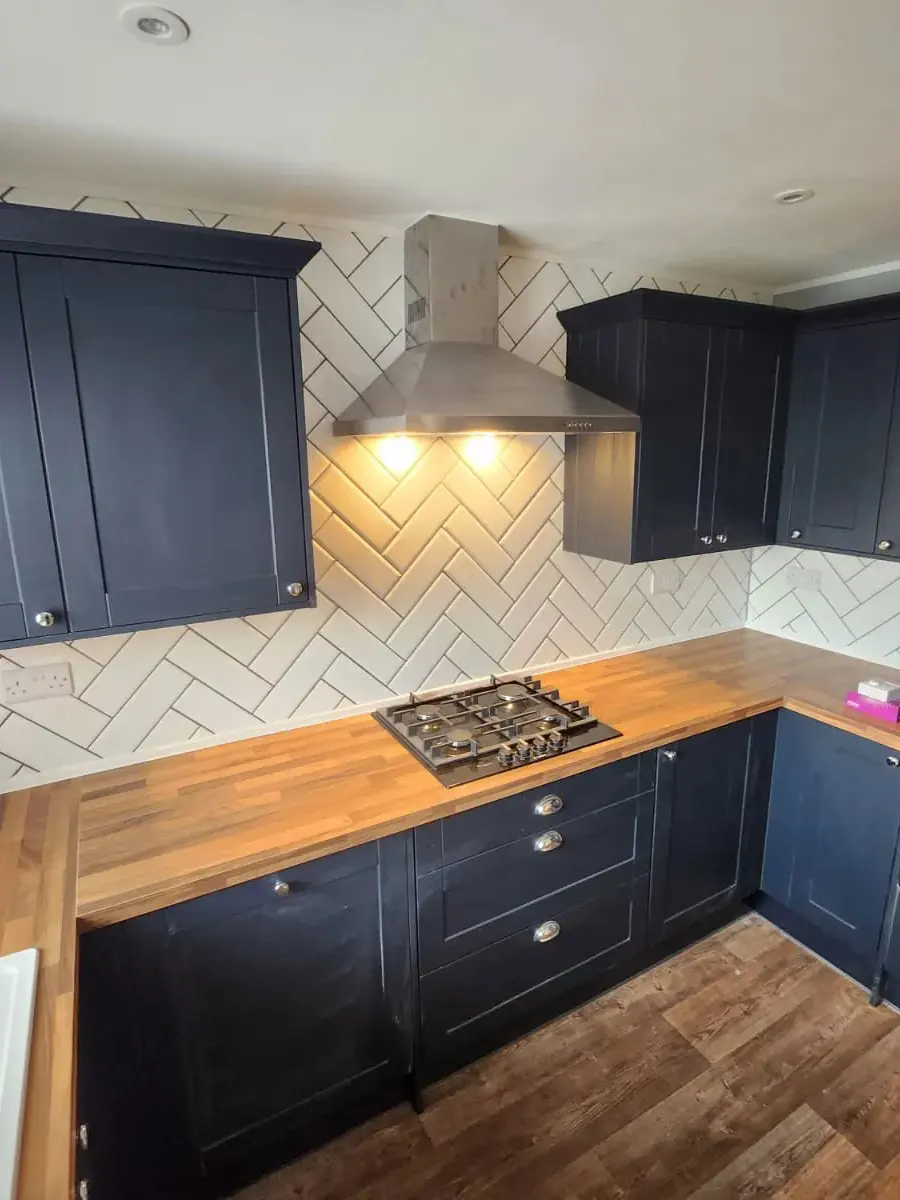 A navy shaker kitchen with a herringbone splashback and oak worktop