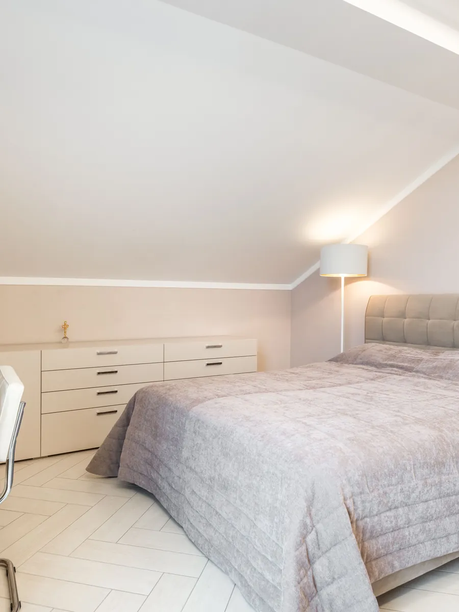 A converted loft bedroom with a sloping ceiling and fitted drawers built into the eaves