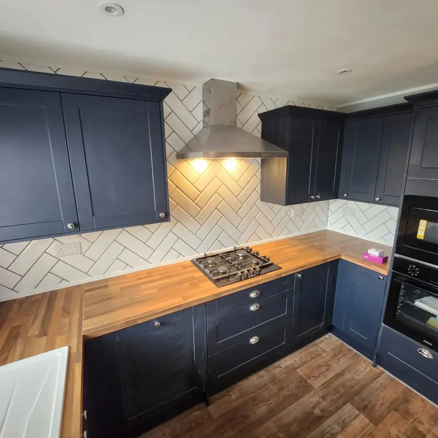 A navy shaker kitchen with a herringbone tiled splashback and oak worktop
