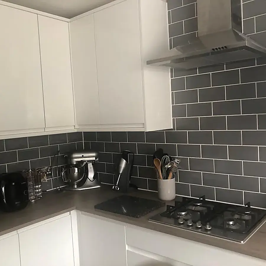 A white gloss kitchen with a gas hob and grey metro tiled splashback
