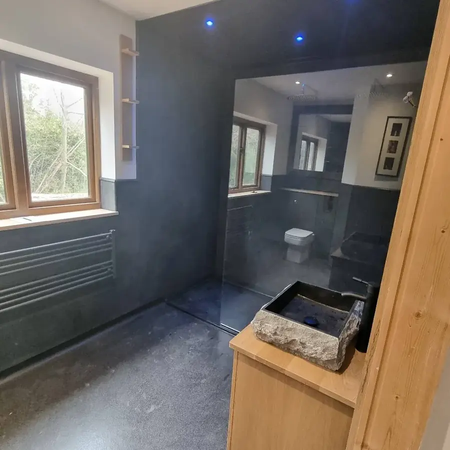 A dark slate tiled bathroom with an oak vanity unit and stone basin