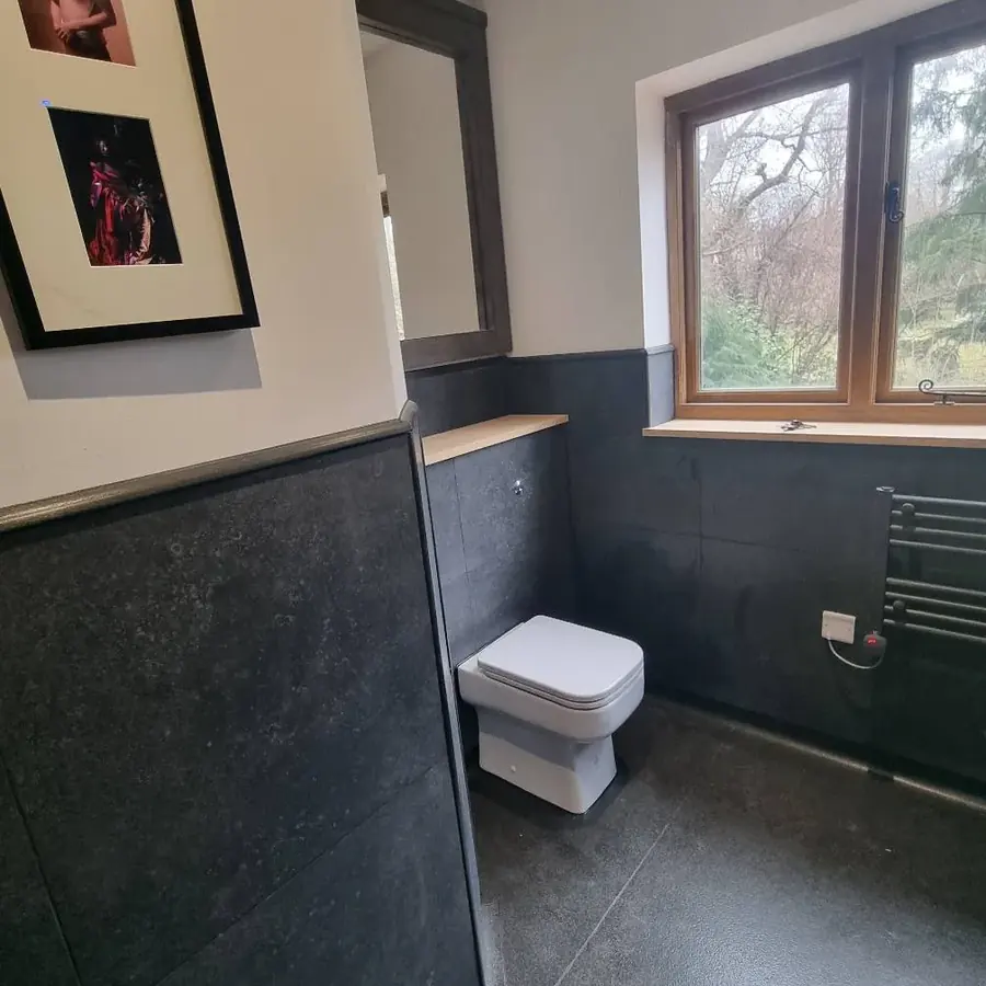 A dark slate tiled bathroom with a heated towel rail and framed prints