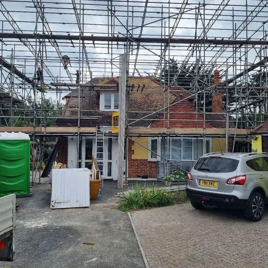 A house under scaffold with a van and skip outside