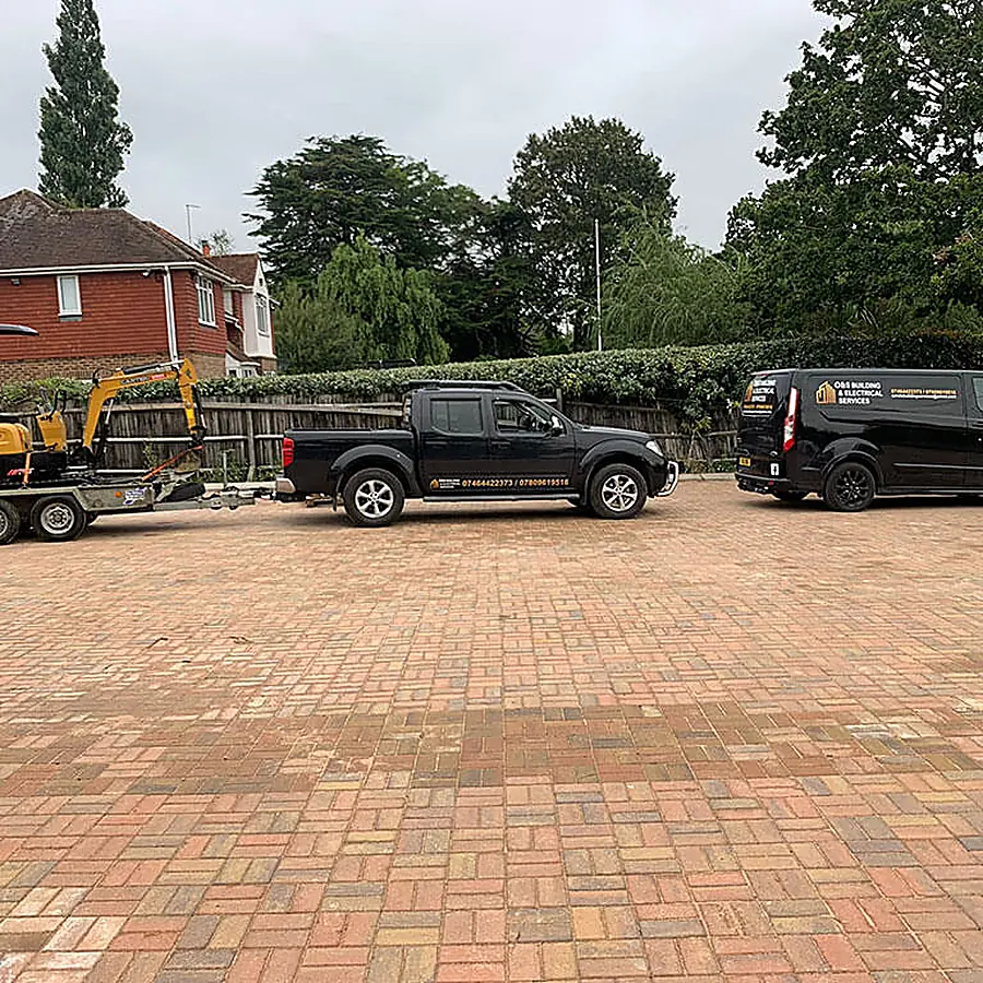 A large red block paved forecourt with vehicles parked