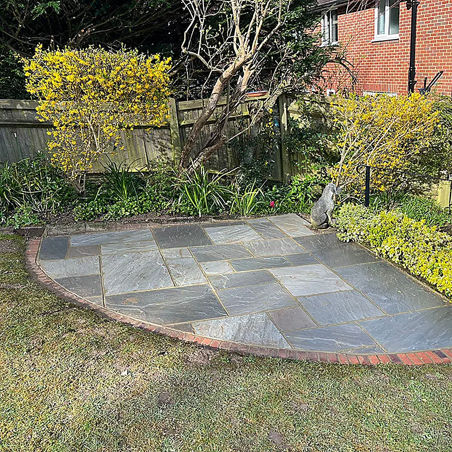 A circular sandstone patio set into a lawn with a brick edge