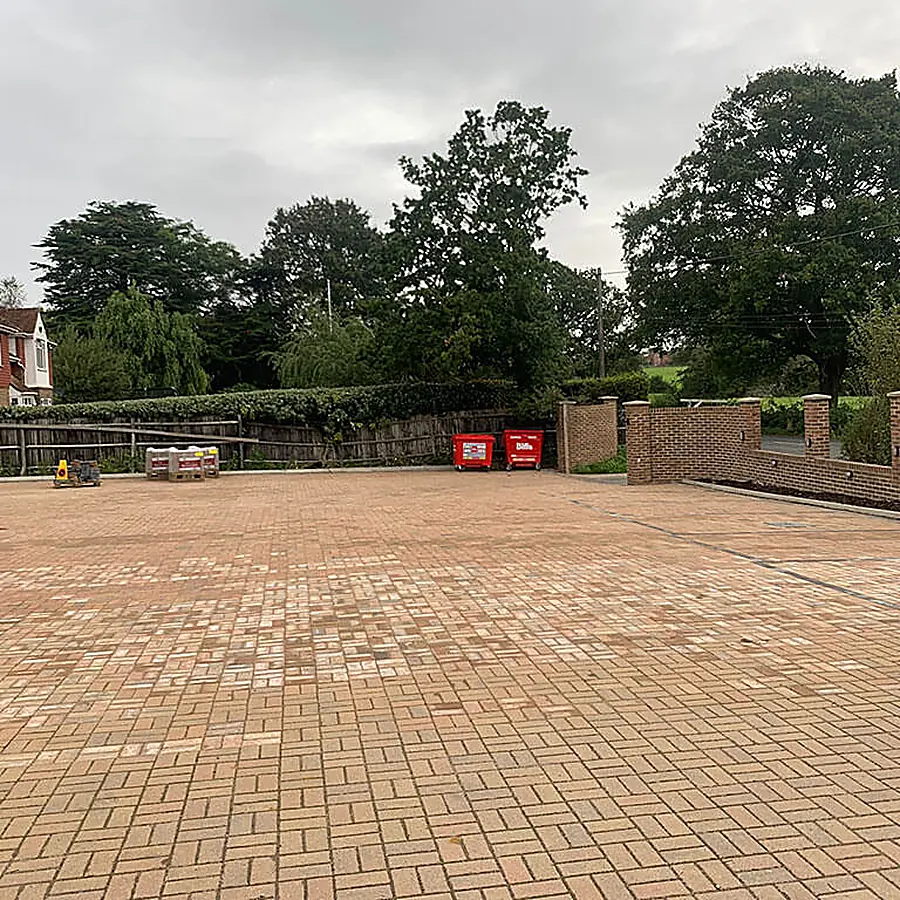 A large block paved parking area with a brick wall boundary