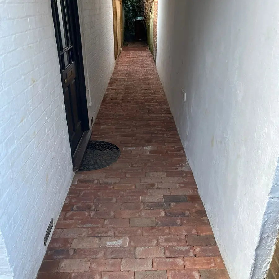 A brick paved side passage between a house and a fence
