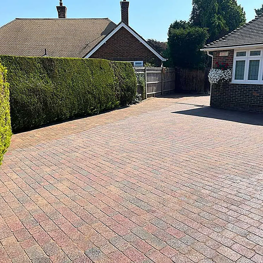 A red block paved driveway beside a hedge
