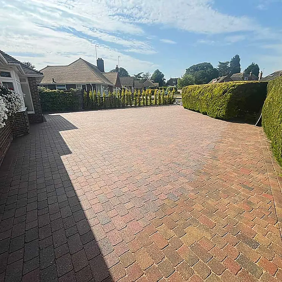 A long block paved driveway between hedges