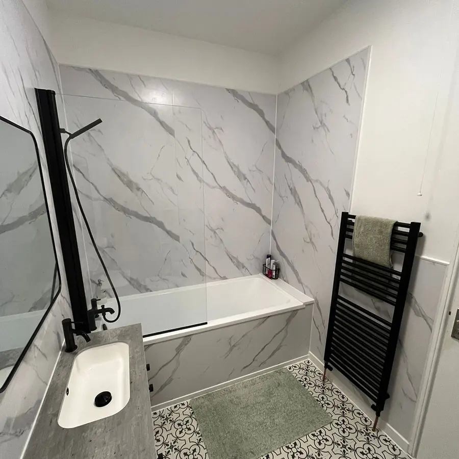 A marble tiled bathroom with a bath and black towel rail